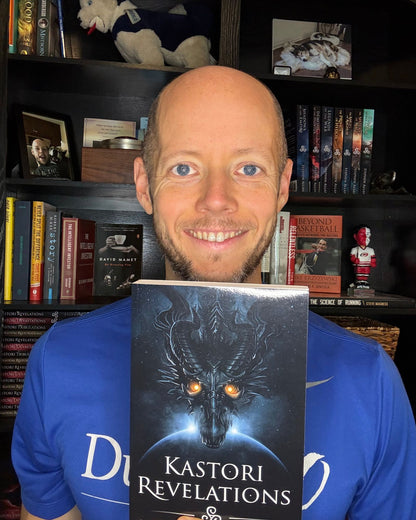 Author Stephen Allan holding a paperback copy of Kastori Revelations in front of his bookshelf