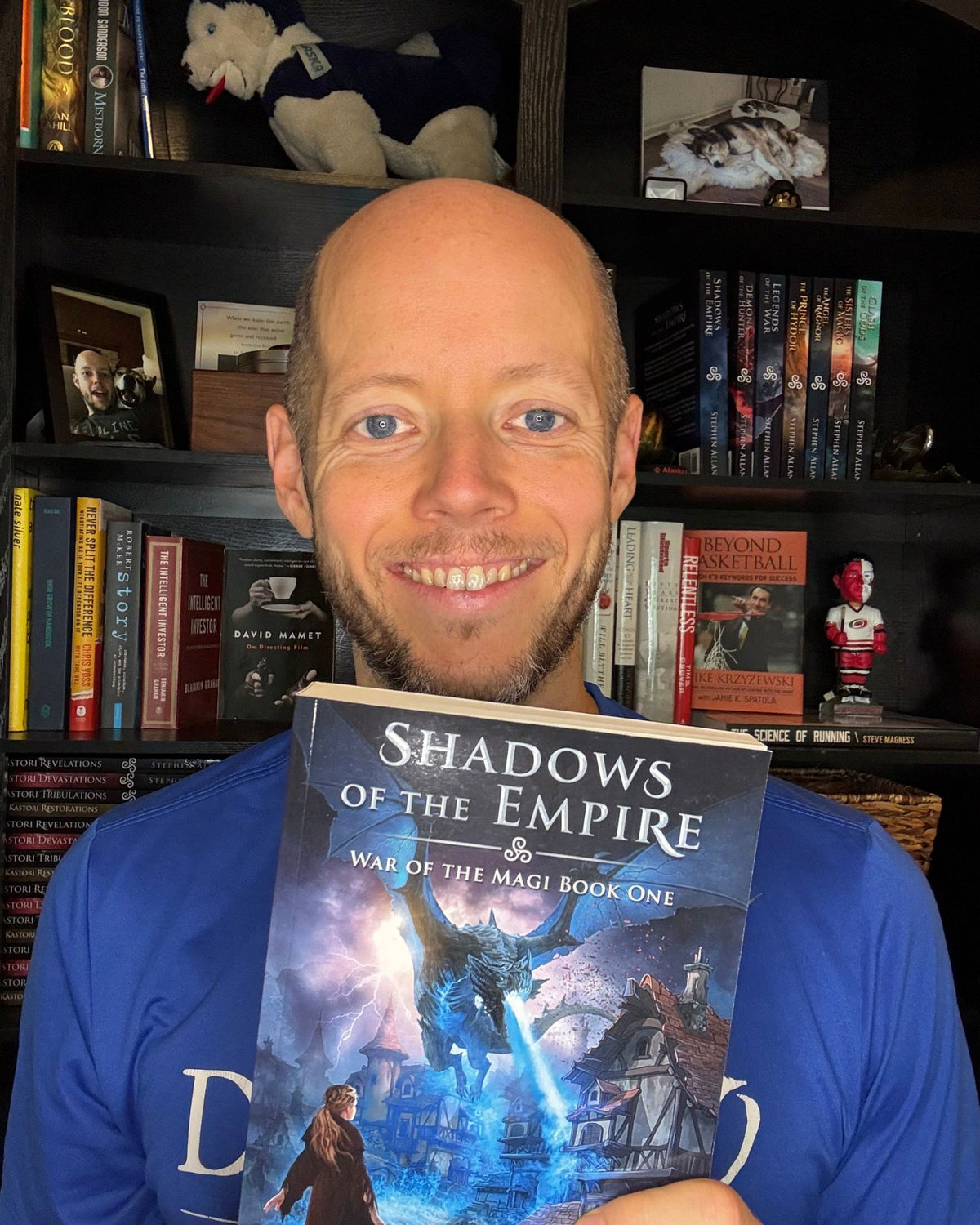 Author Stephen Allan holding a paperback copy of Shadows of the Empire in front of his bookshelf